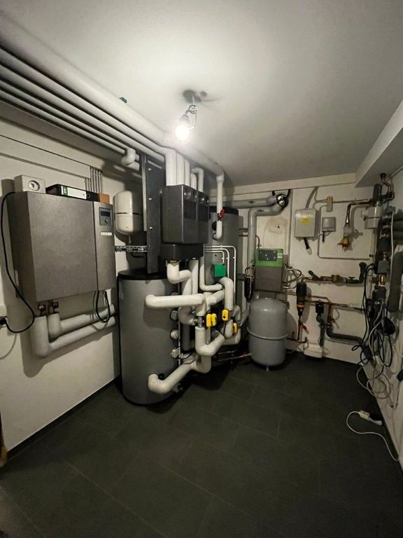 Keller mit Heizungsanlage, einschließlich Tanks, Rohren und Schaltschränken. Grau- und Weißtöne dominieren.