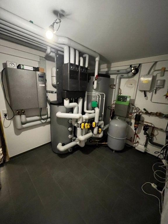 Ein Kellerraum mit Heizungs- und Wassersystemen: Tanks, Rohre und Schalttafeln.