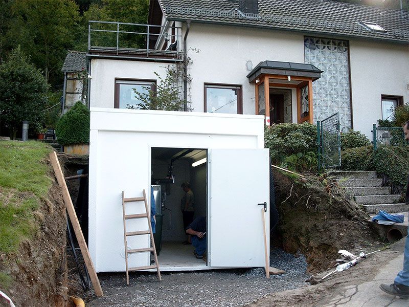 Ein Mann sitzt in einem kleinen weißen Gebäude vor einem Haus.