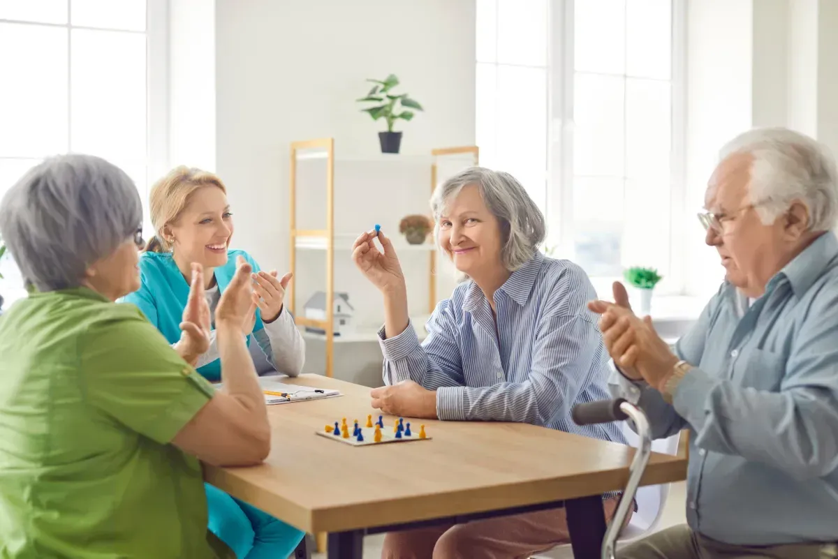 Cuatro adultos mayores jugando a un juego de mesa, sonriendo e interactuando alrededor de una mesa