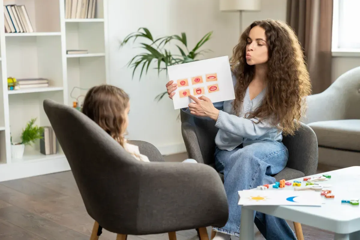 Mujer mostrando un cuadro de sonidos del habla a un niño en una sesión de terapia.