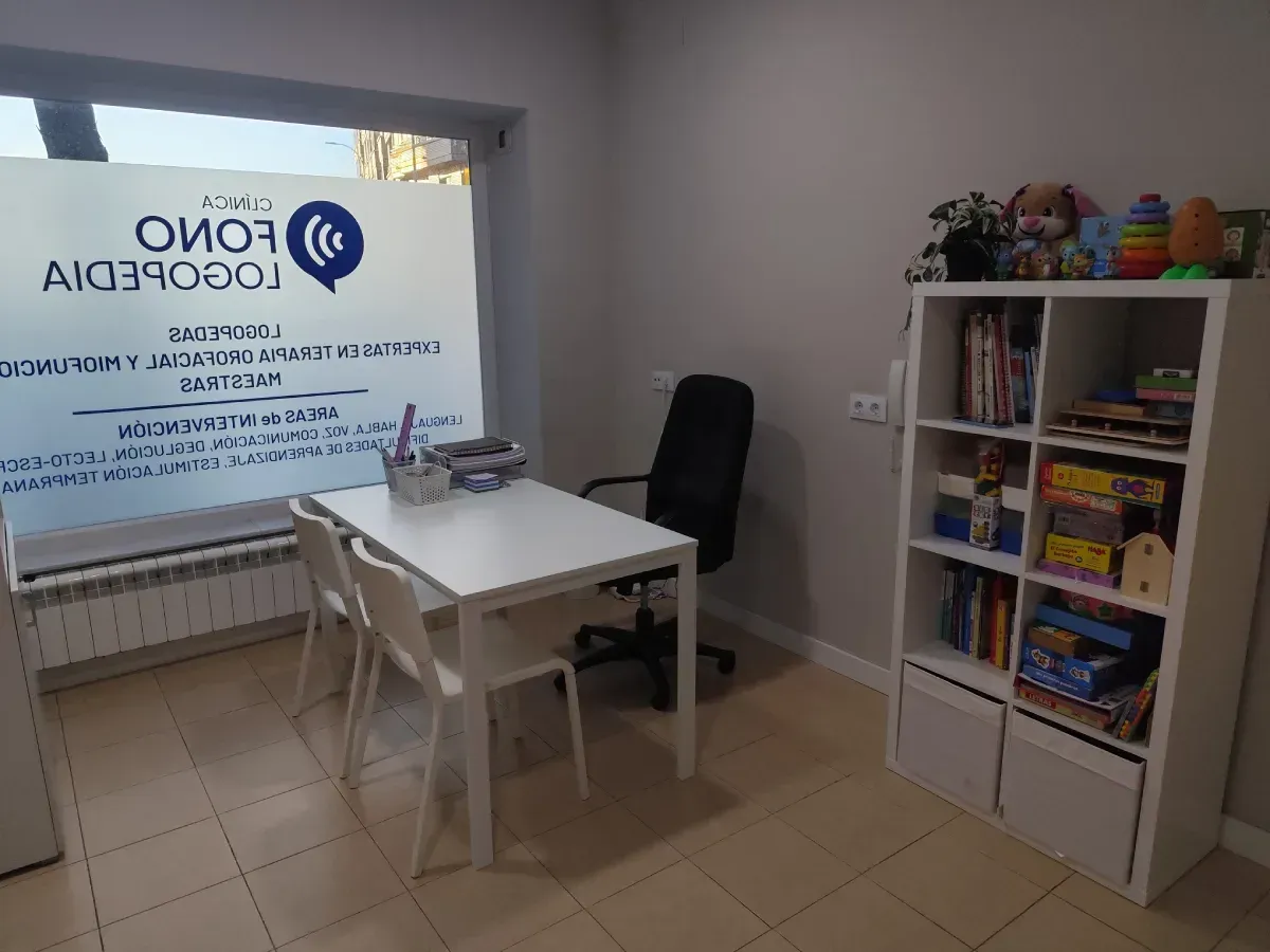 Espacio de oficina con mesa, sillas, estanterías y ventana con logotipo.