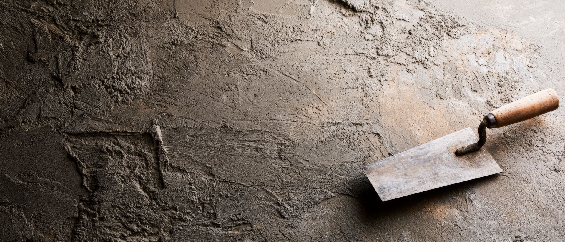 Lissage à la truelle du béton humide sur une surface de sol grise et rugueuse.