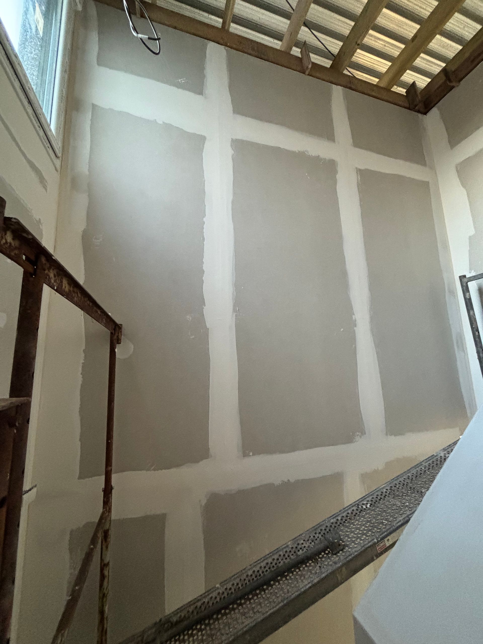Échafaudages à l'intérieur d'une pièce aux cloisons sèches non finies et au plafond à poutres apparentes en bois.