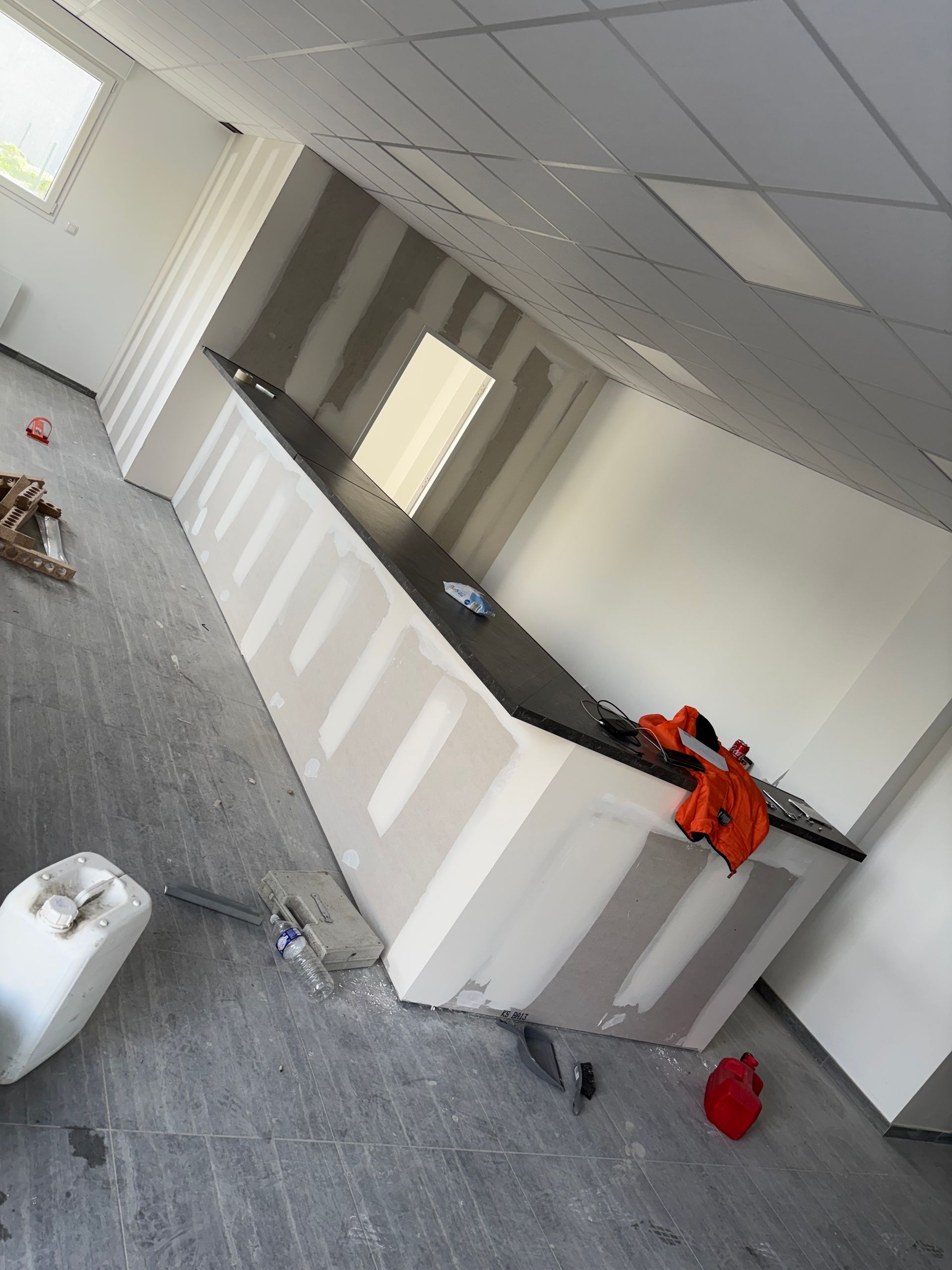 Espace d'accueil vide avec une moquette grise, des murs blancs et une veste orange sur le comptoir.