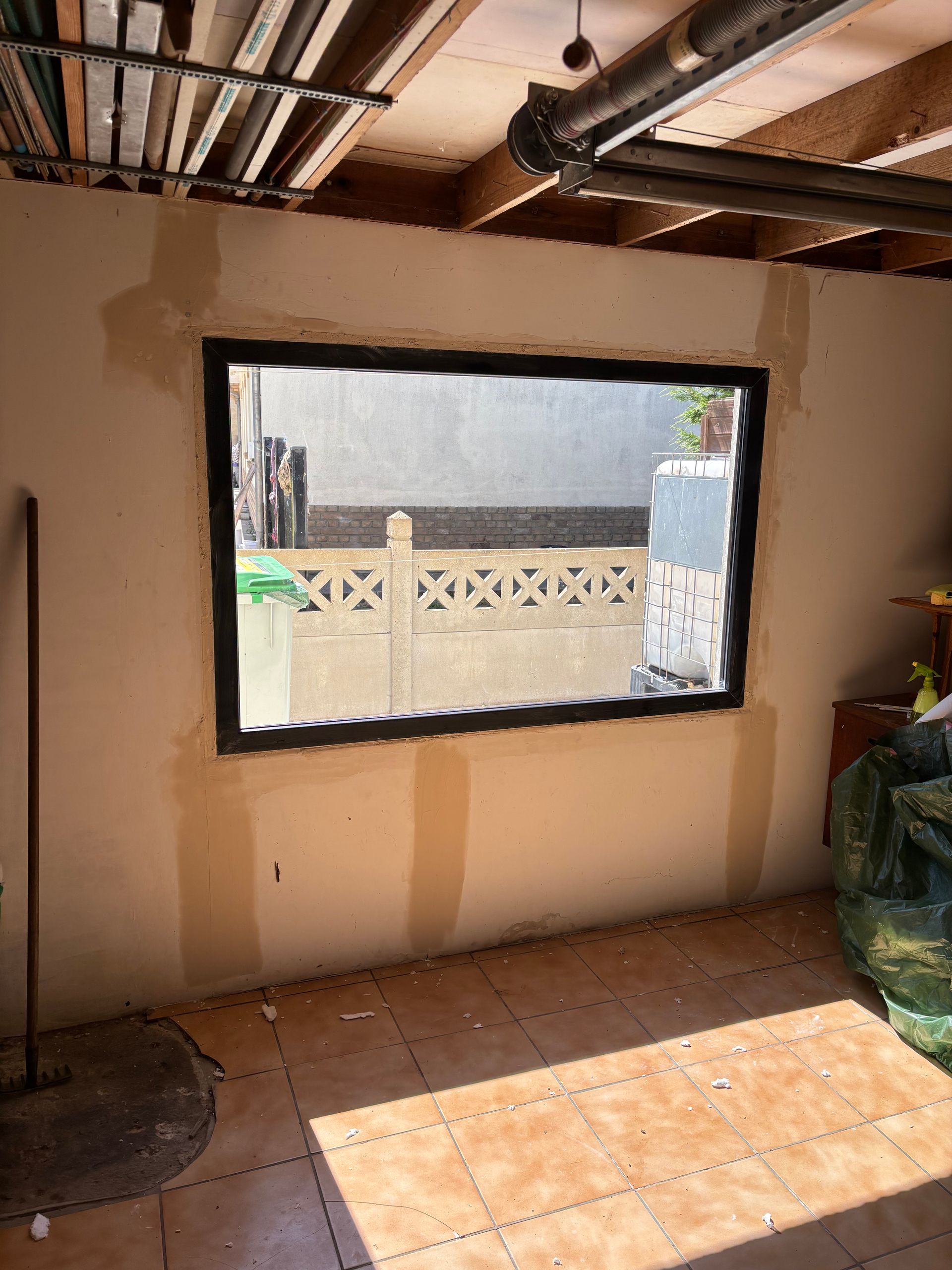 Mur intérieur percé d'une fenêtre rectangulaire offrant une vue dégagée sur l'extérieur et un sol carrelé en dessous.