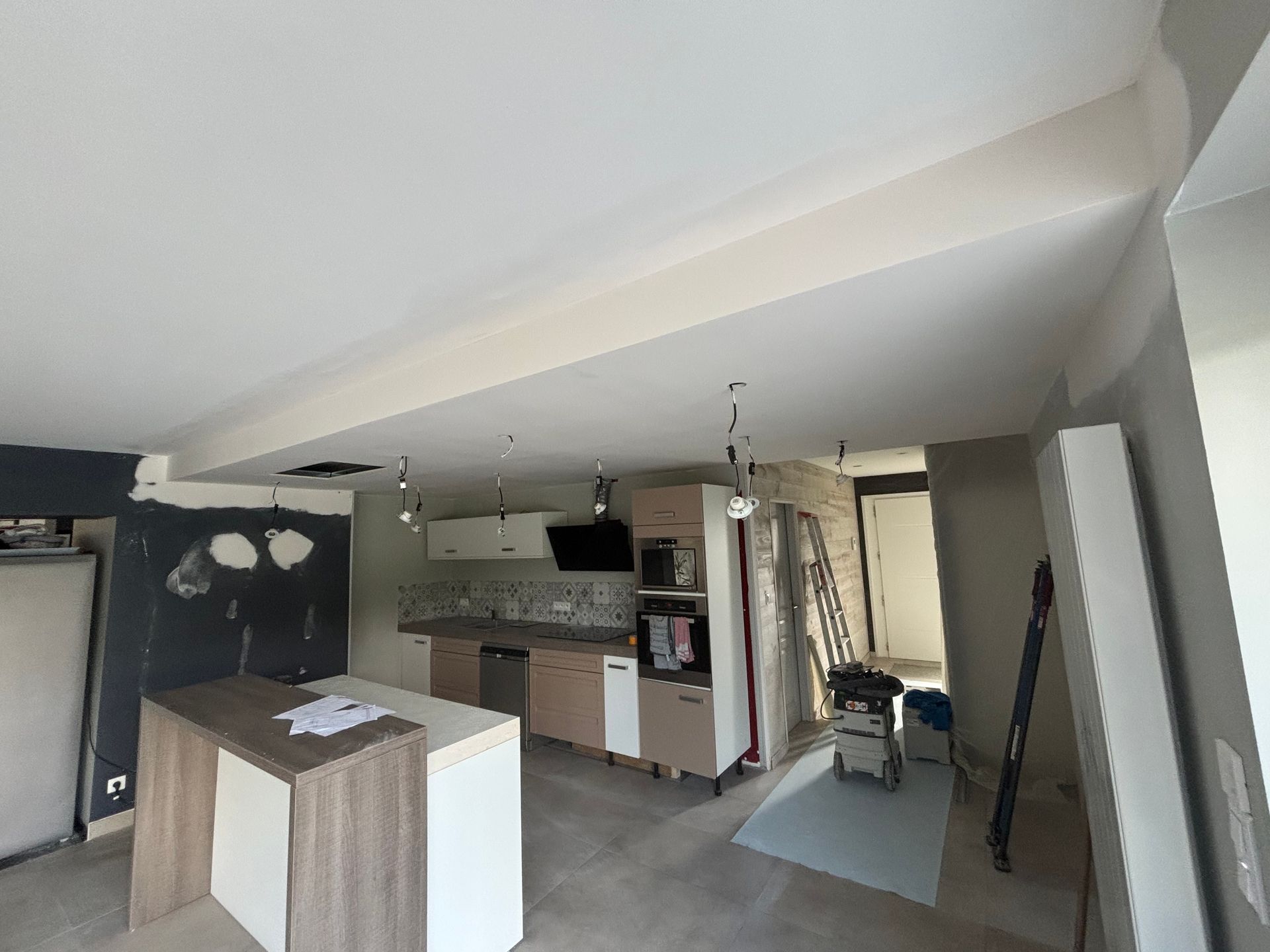 Cuisine et séjour ouverts en cours de rénovation avec poutres apparentes, placards et matériaux de construction apparents.