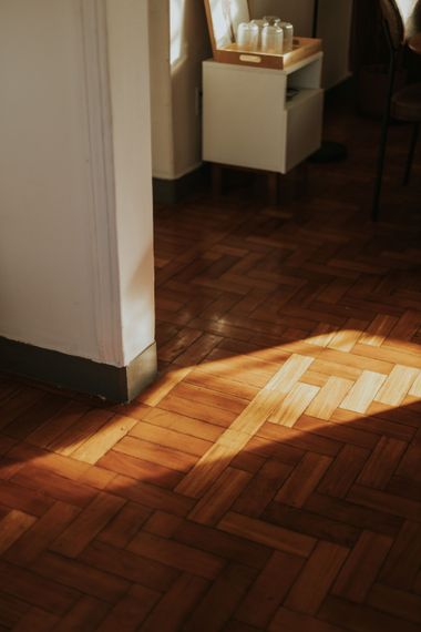 Couloir baigné de lumière naturelle avec un parquet à chevrons et une petite armoire blanche contre le mur.