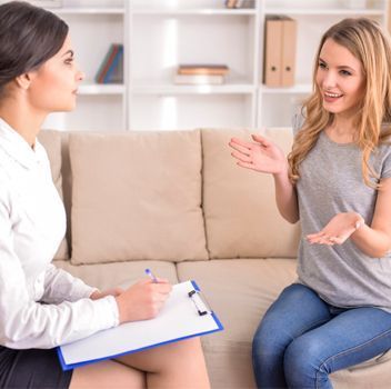 Una mujer está sentada en un sofá hablando con una psicóloga.