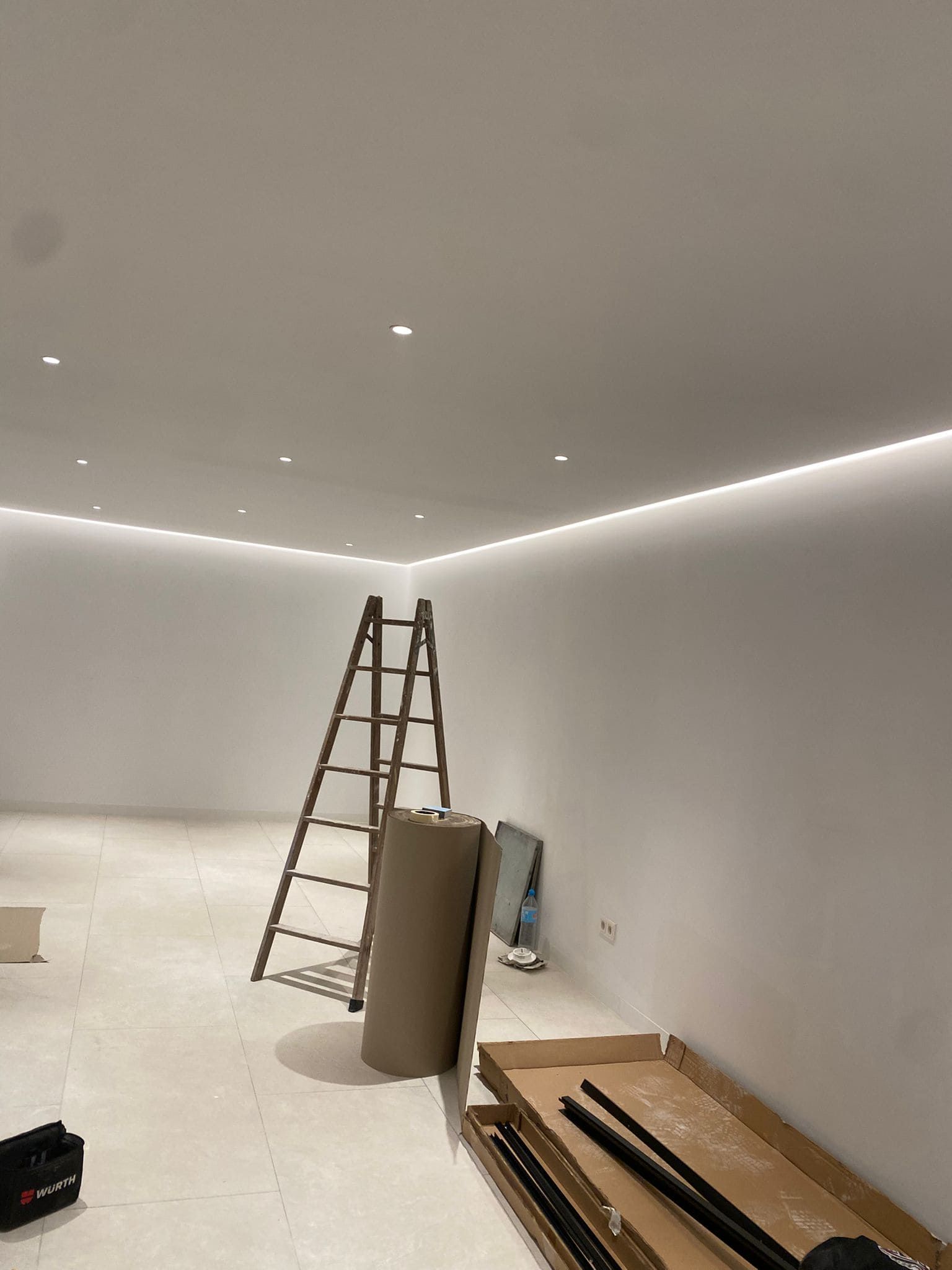 Habitación vacía con iluminación empotrada instalada y una escalera, materiales de construcción en el piso.