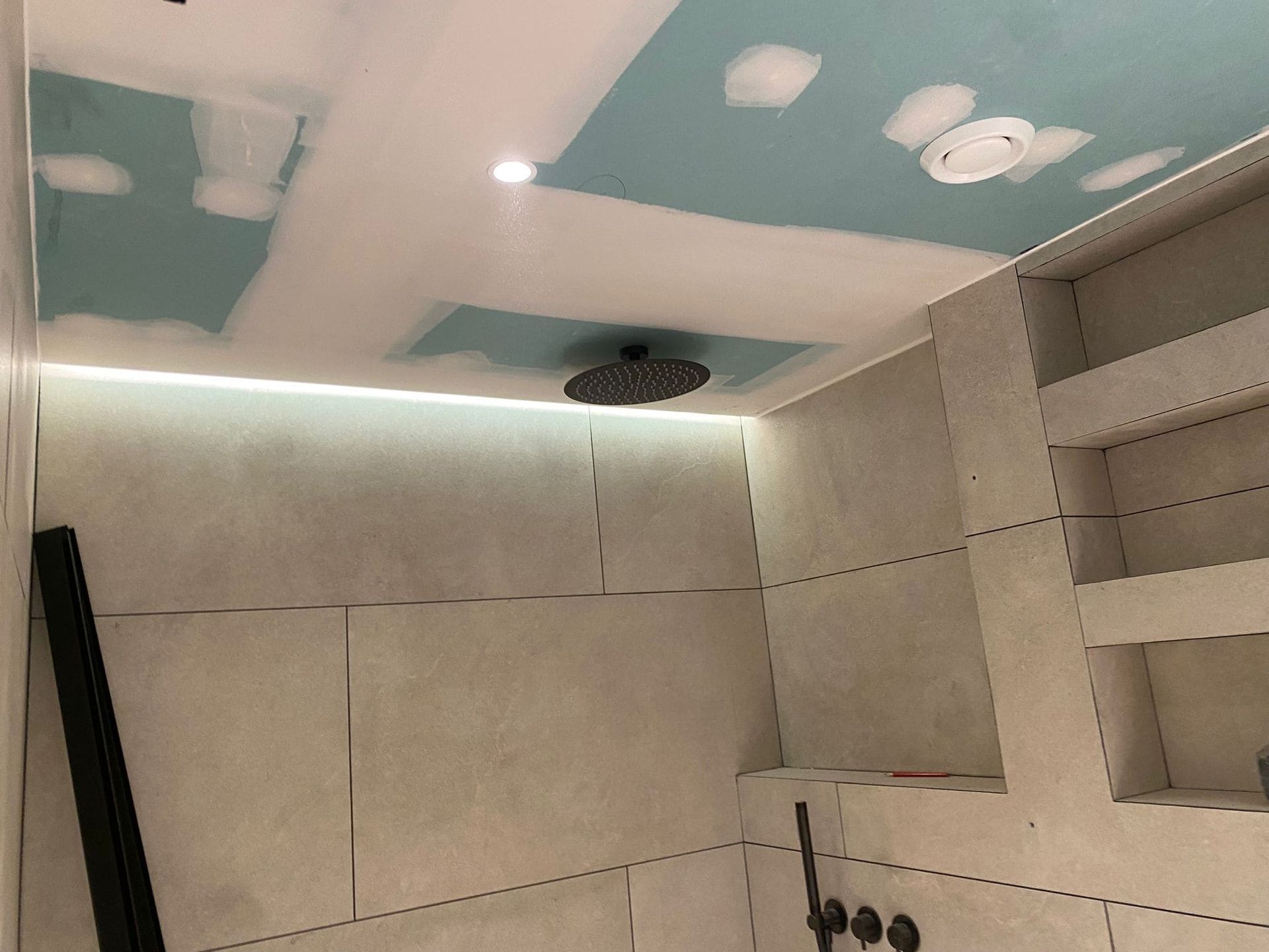 Renovación de baño en progreso; cabezal de ducha, iluminación empotrada, paredes y techo parcialmente terminados.