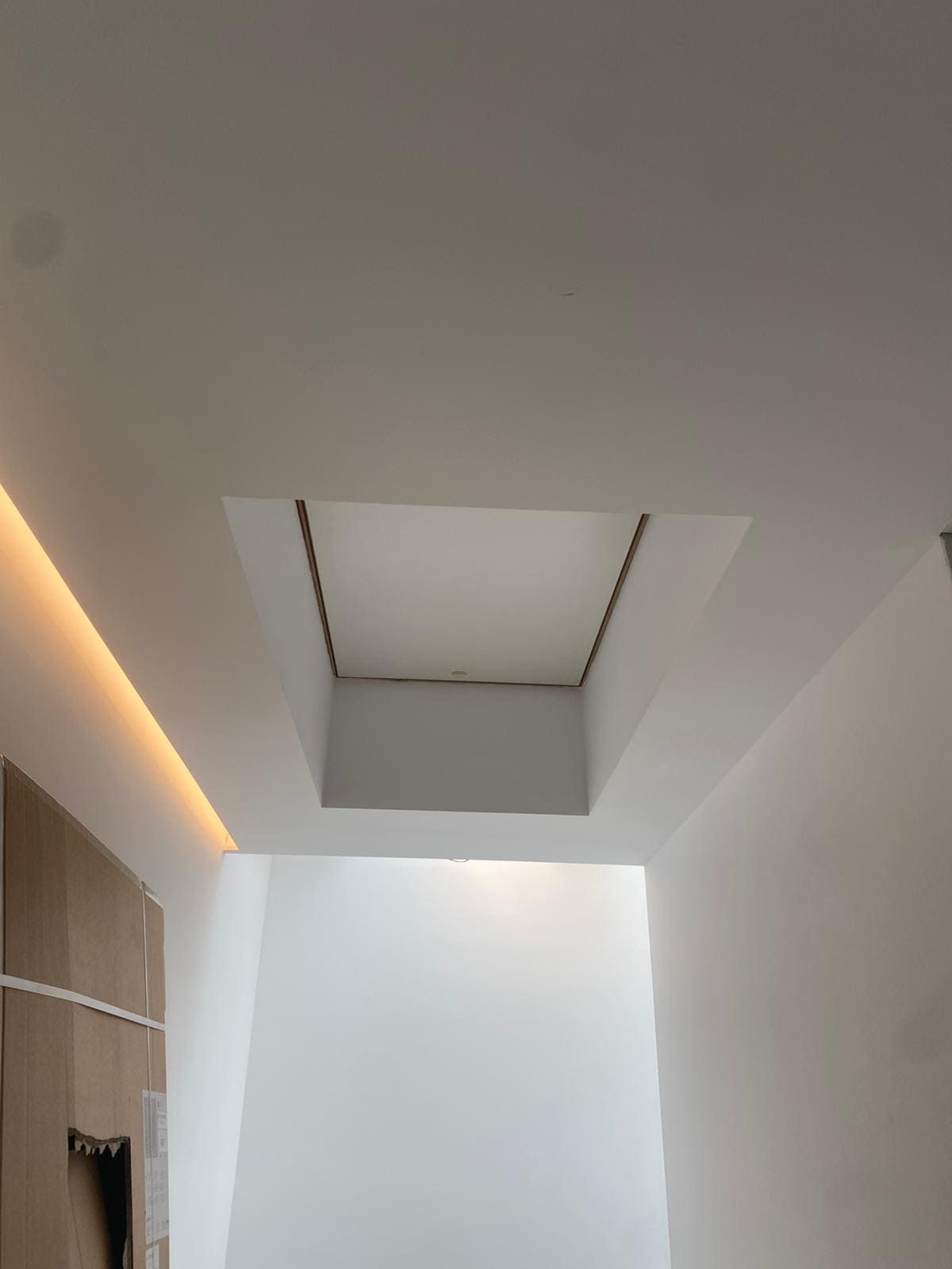 Techo con abertura cuadrada empotrada. Paredes blancas, luz empotrada y armario de madera visible.