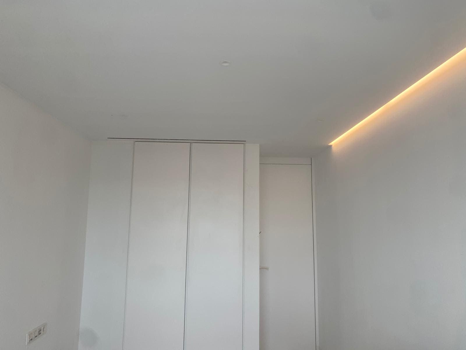 Paredes y techo blancos con puertas de armario empotradas y tiras de iluminación.