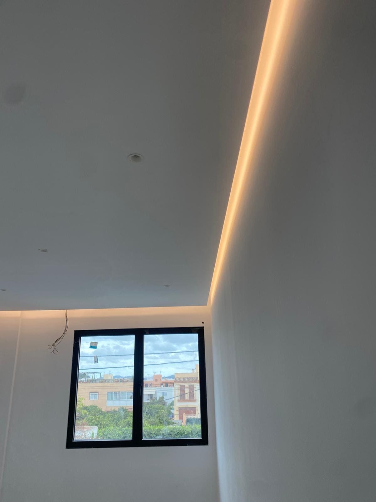 Una habitación moderna con ventana. Techo iluminado, paredes neutras y vistas a los edificios.