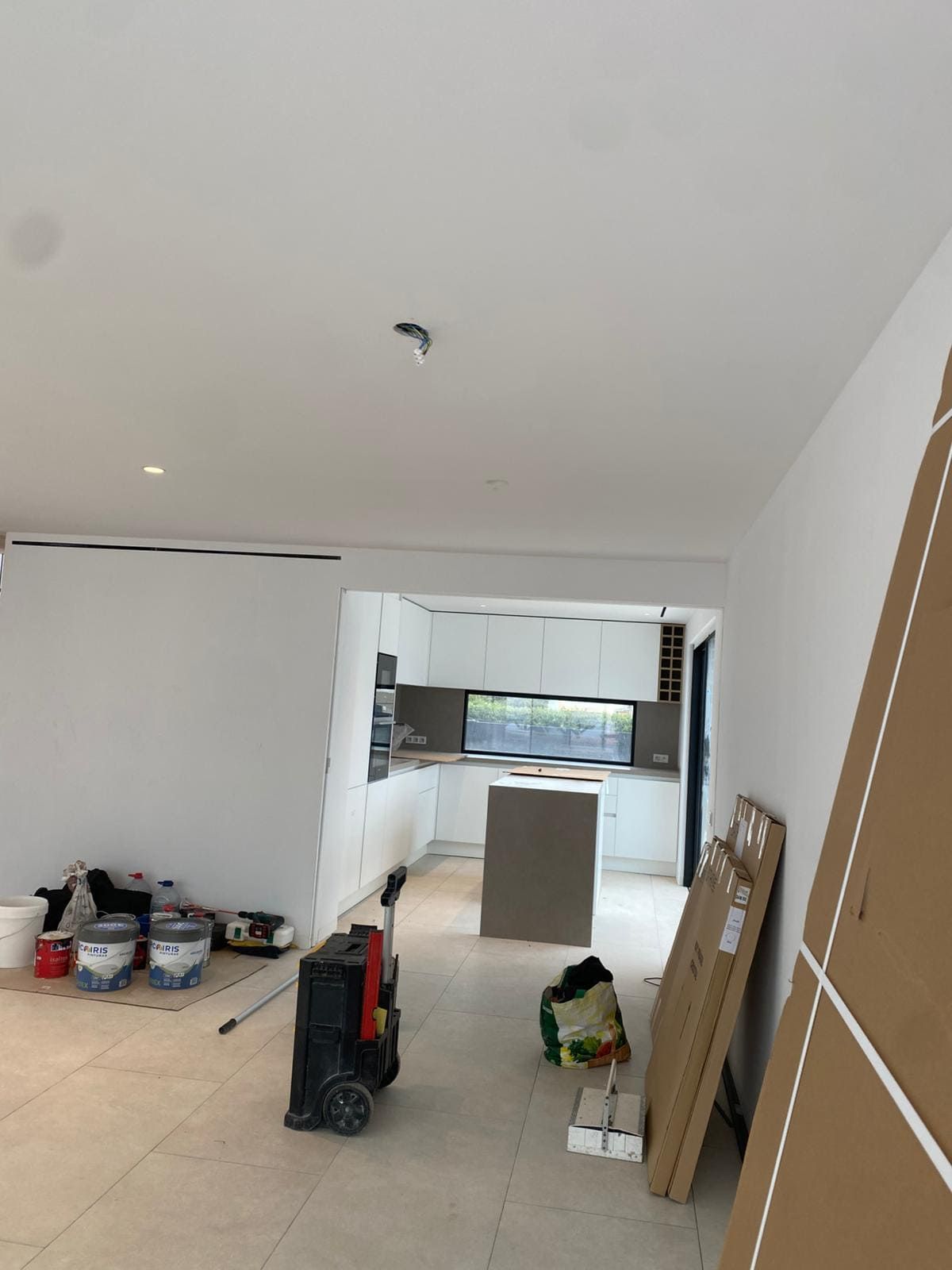 Vista interior de una cocina en remodelación, con paredes blancas, gabinetes y una isla central.