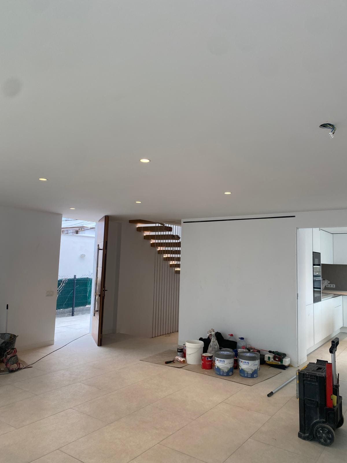 Interior de una casa en construcción; paredes blancas, luces empotradas, escaleras de madera.