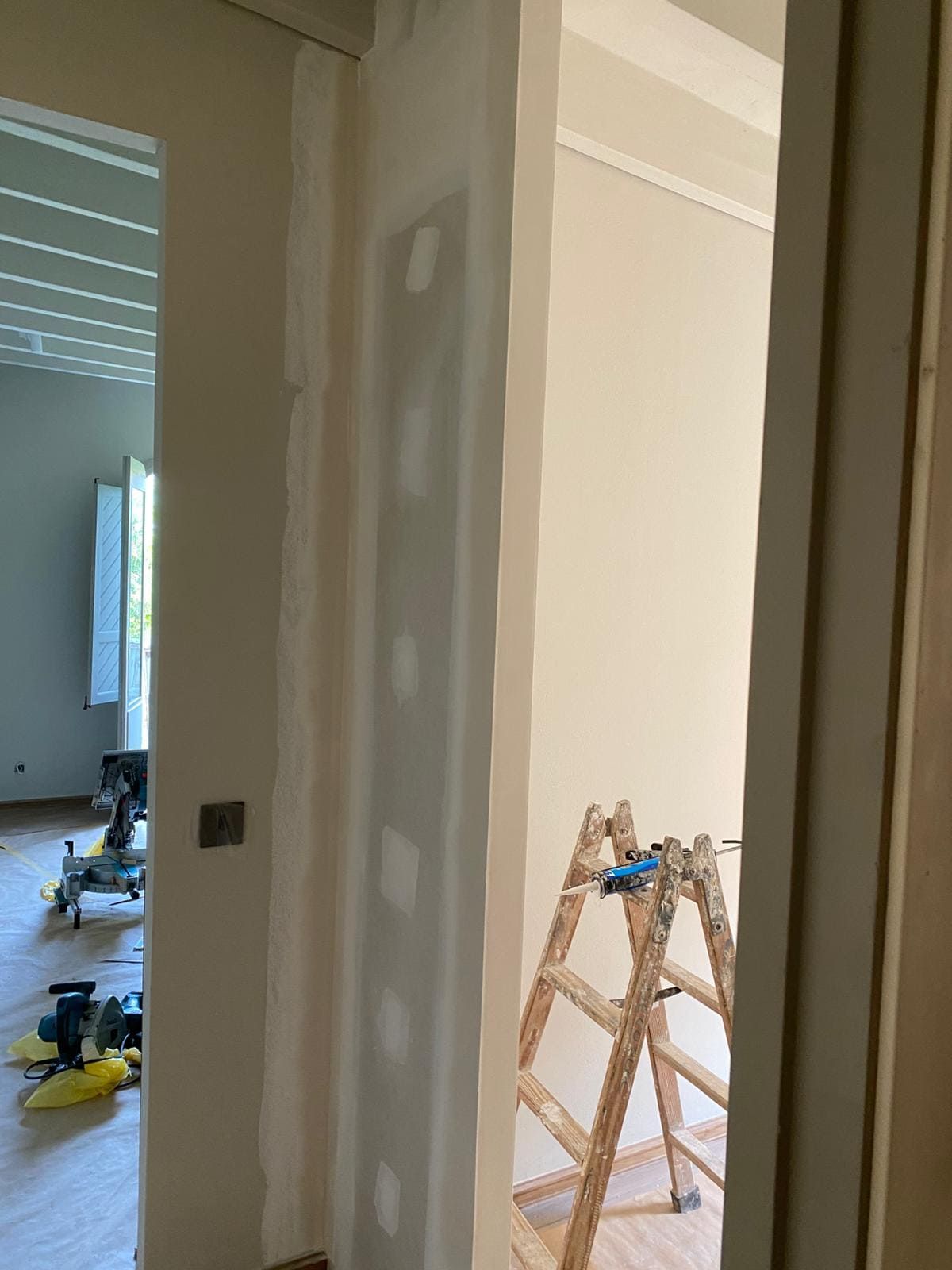 Puerta interior en construcción; paneles de yeso y escalera visibles. Paredes beige claro.