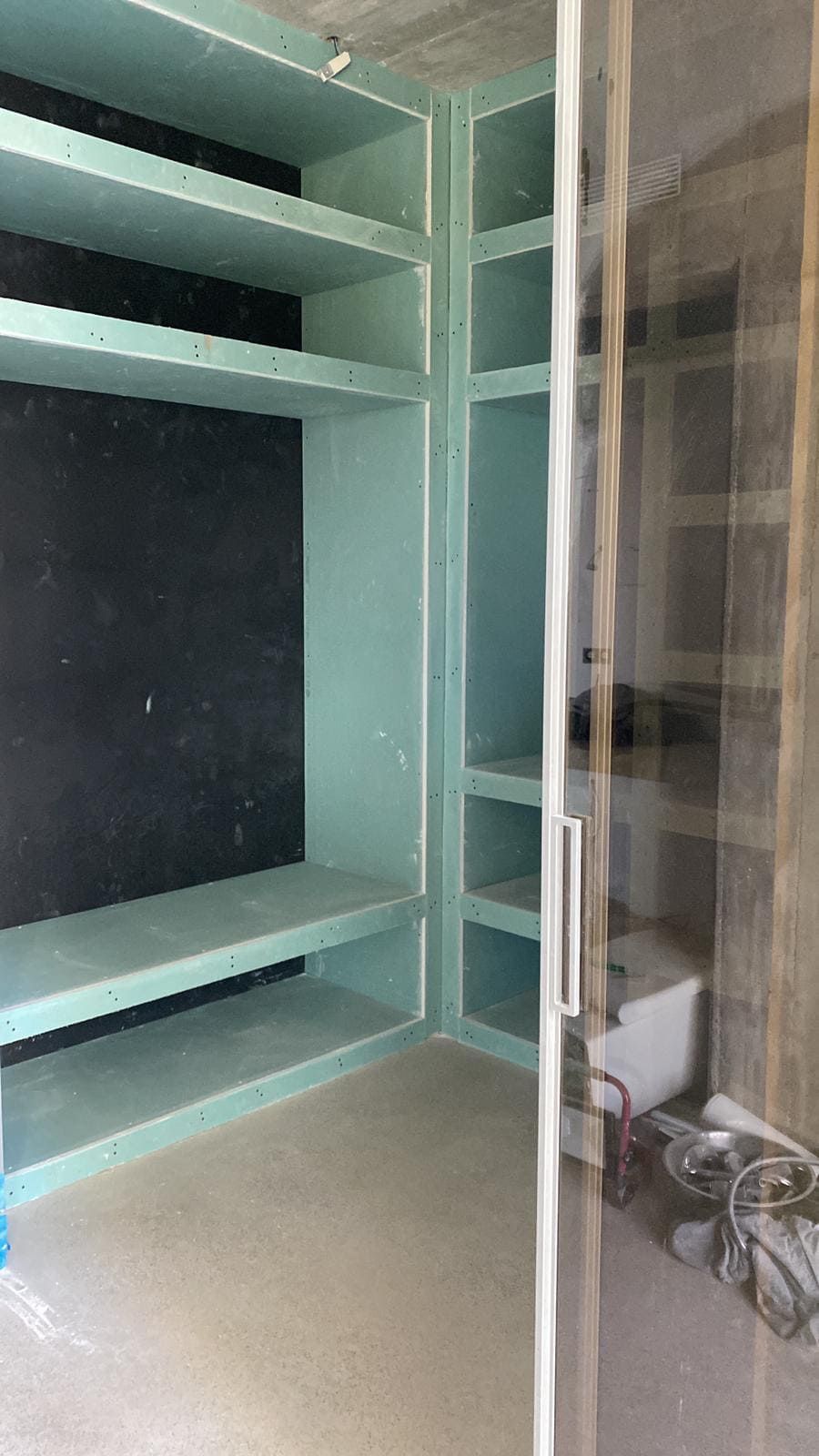 Estantería empotrada con múltiples baldas. Paneles de yeso pintados de verde claro. Habitación parcialmente construida.