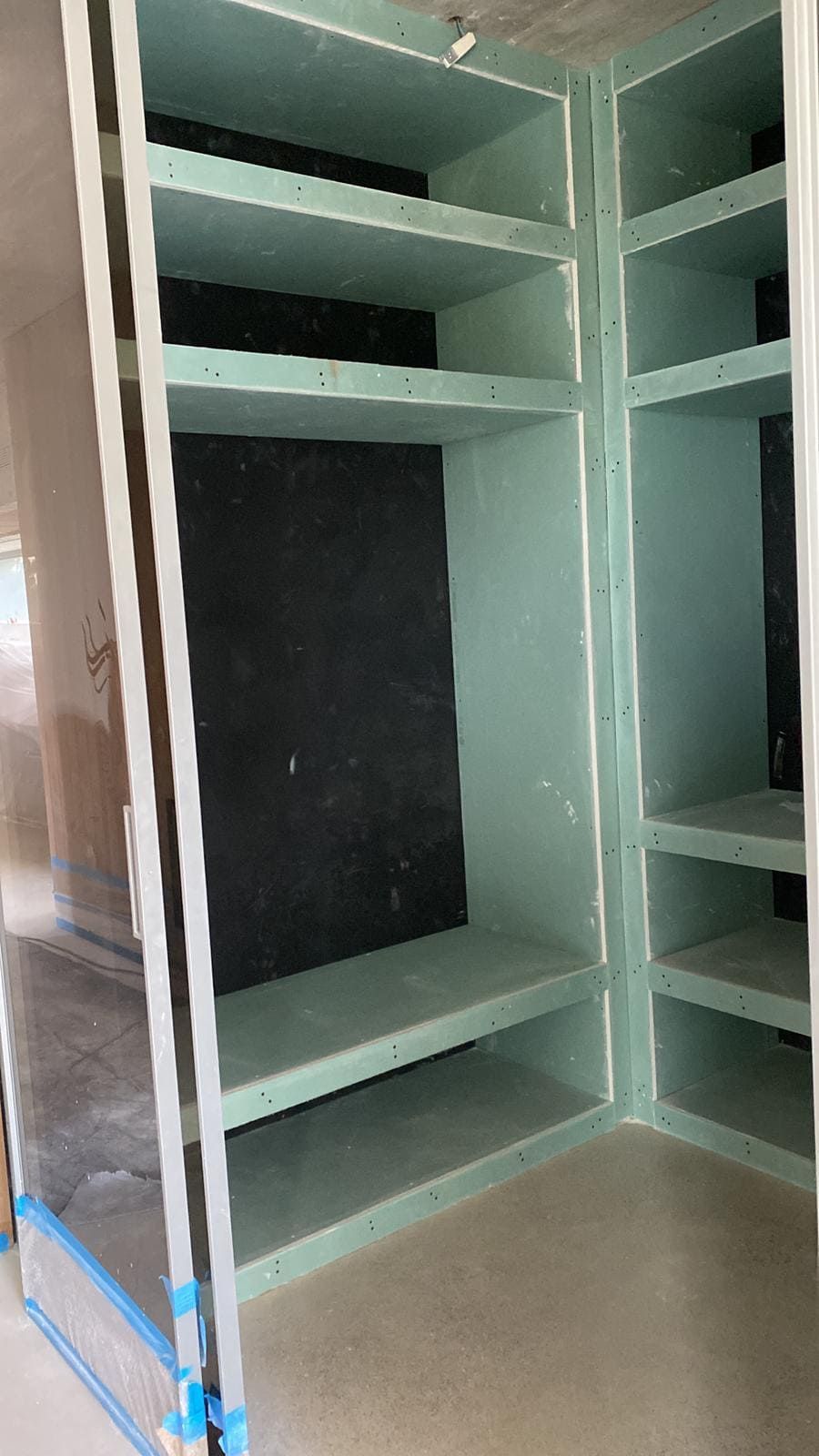 Estantes empotrados sin terminar en una esquina, construidos con paneles de yeso verde. La parte trasera está revestida con material negro.