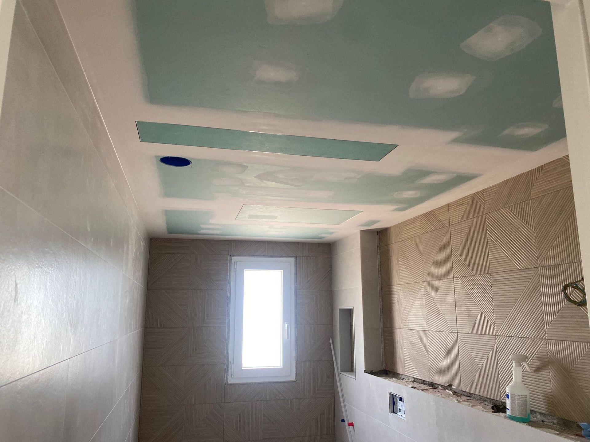 Baño en construcción, con techo de drywall a la vista y pared texturizada.