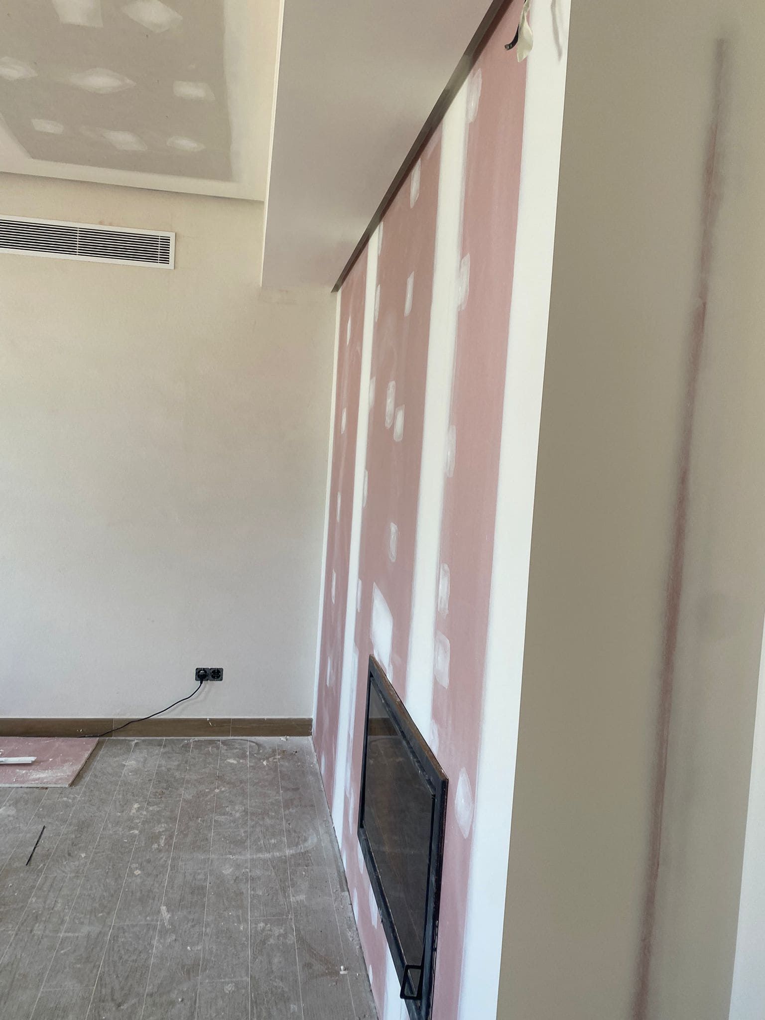 Pared de yeso con chimenea empotrada. El panel de yeso sin terminar tiene juntas selladas y un marco oscuro para la chimenea.