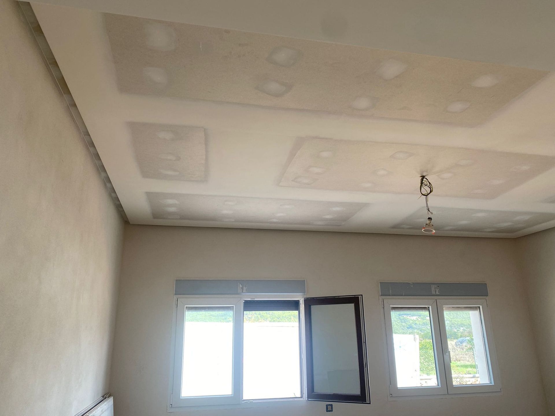 Una habitación moderna con ventana. Techo iluminado, paredes neutras y vistas a los edificios.