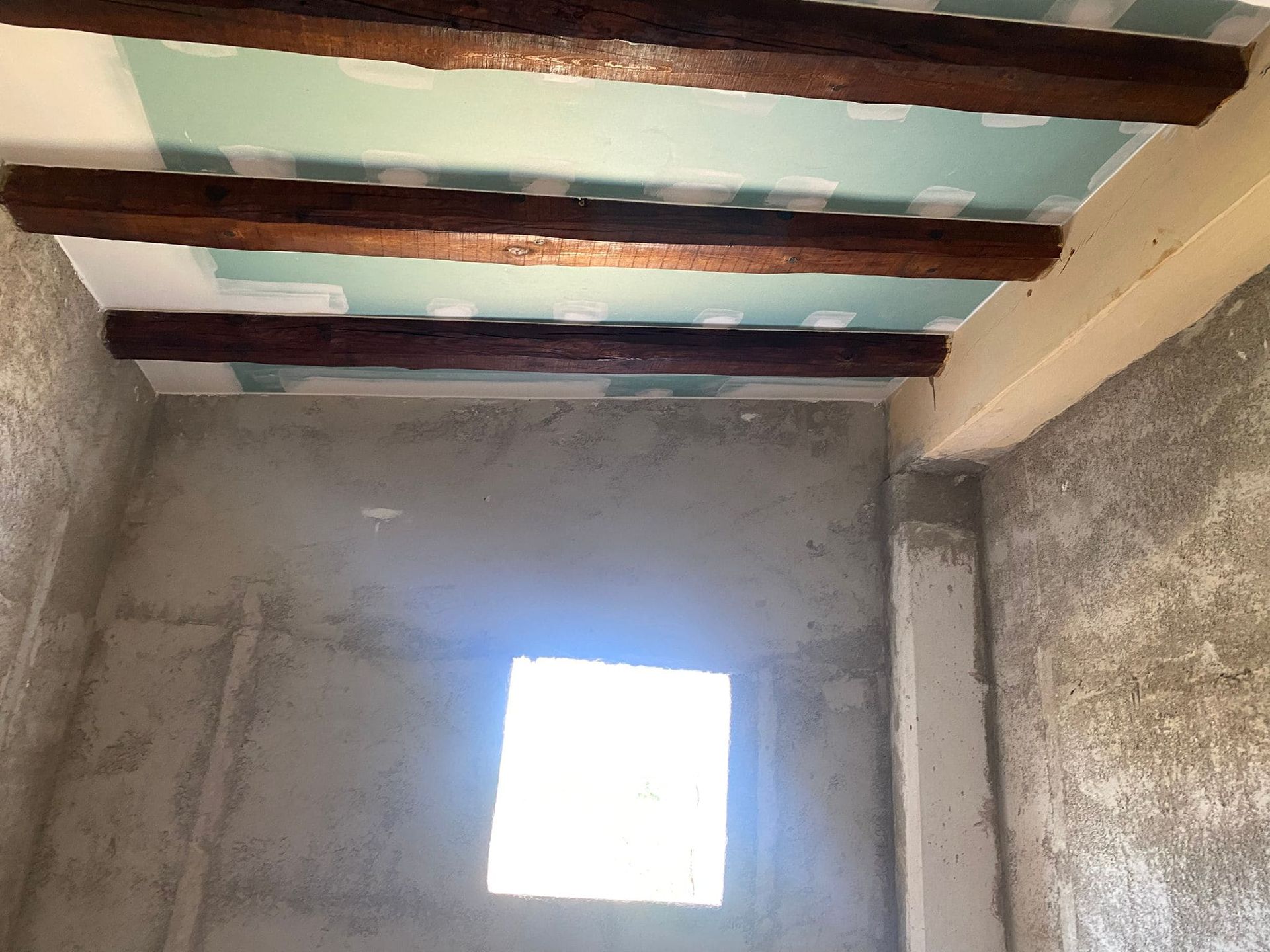 Habitación interior en construcción con andamios, techo dañado y claraboya. Paredes blancas.