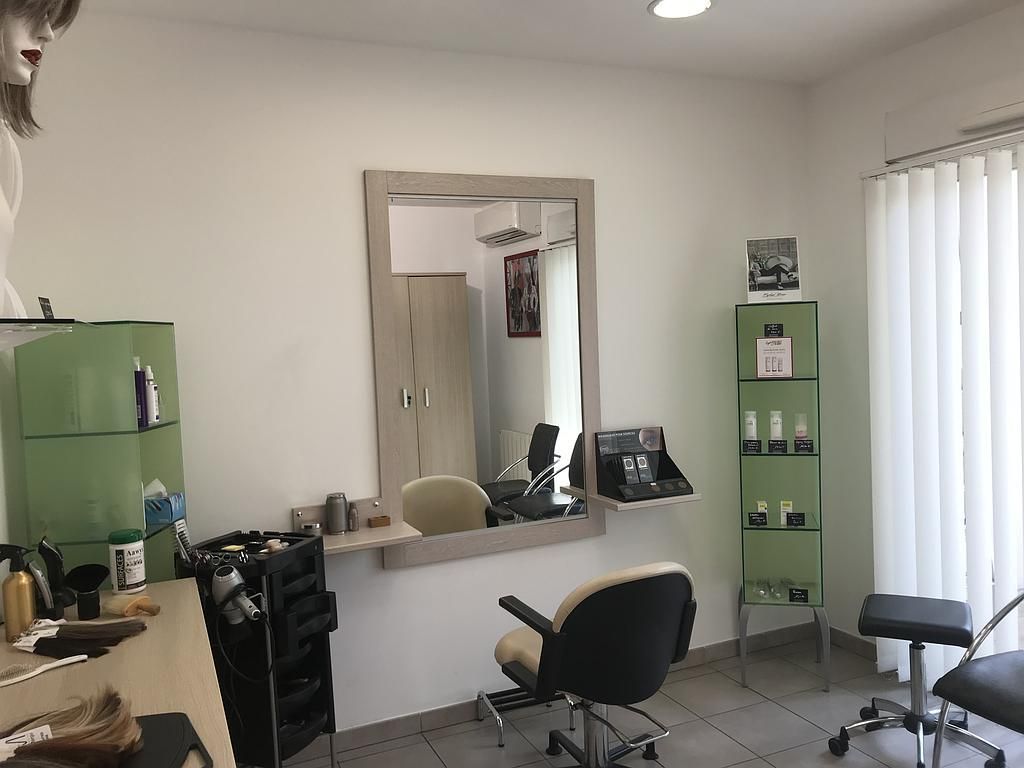Intérieur d'un salon de coiffure avec un grand miroir, des chaises et des étagères présentant des produits.