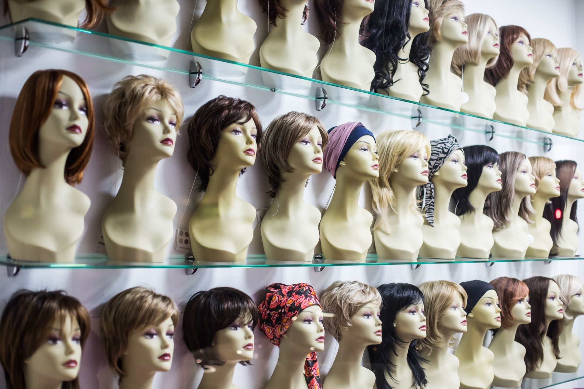 Des rangées de têtes de mannequin présentent diverses perruques sur des étagères.