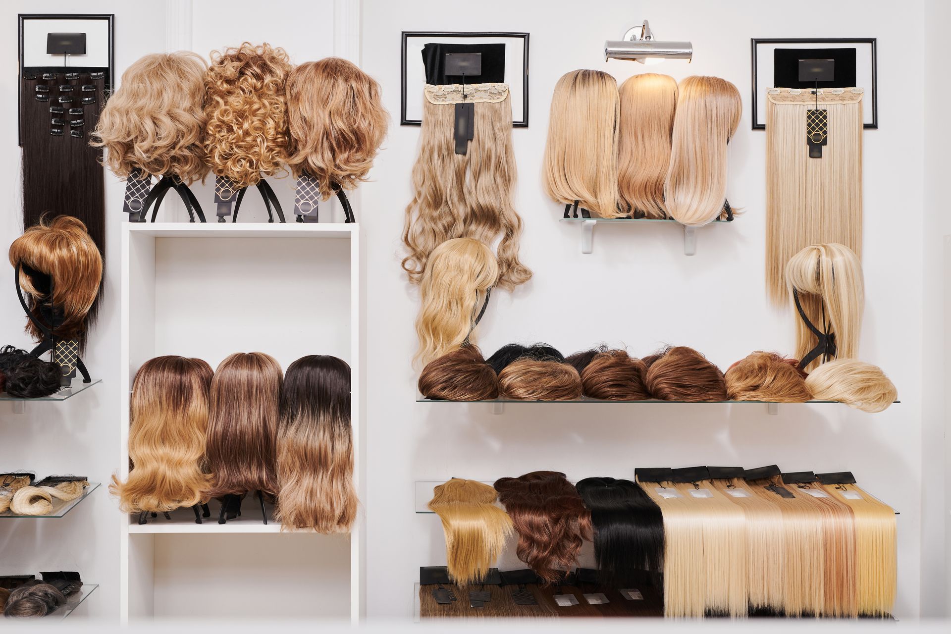 Des perruques de couleurs et de styles variés sont exposées sur des étagères et suspendues à des portants dans une boutique bien éclairée.