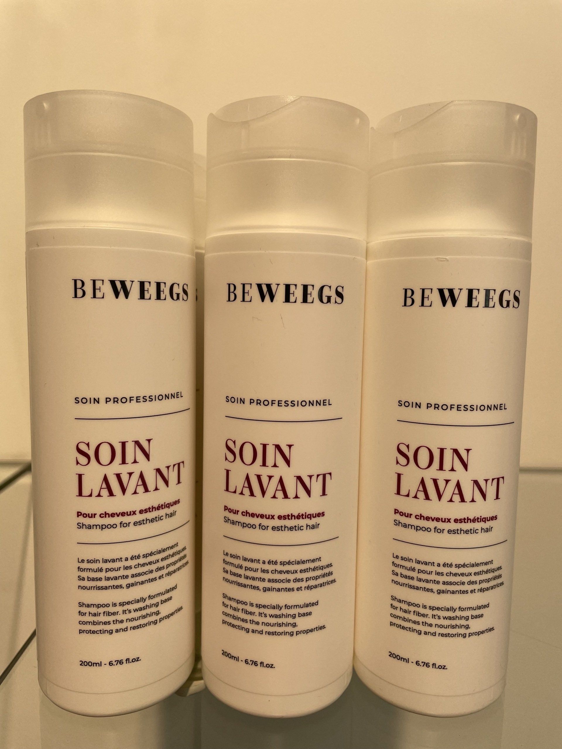 Trois flacons cylindriques blancs portant l'inscription Soin Lavant en violet clair.