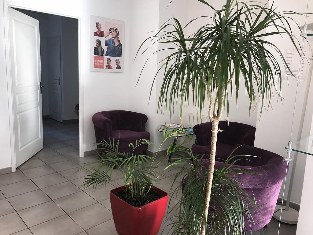 Espace d'accueil avec des chaises violettes, des plantes et une affiche ; des murs blancs et une porte.