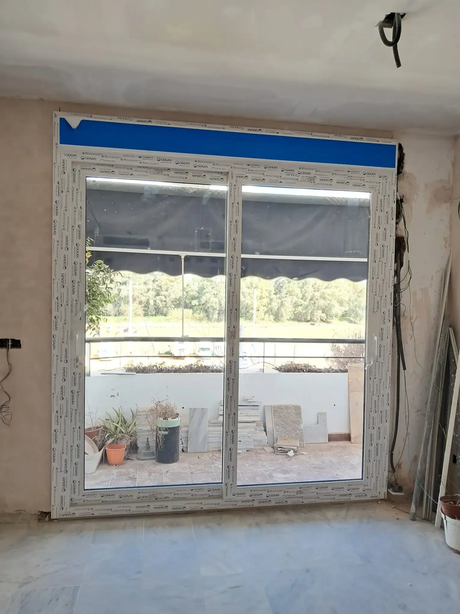 Gran ventana blanca con dos paneles de vidrio y cinta azul instalada en un interior sin terminar.