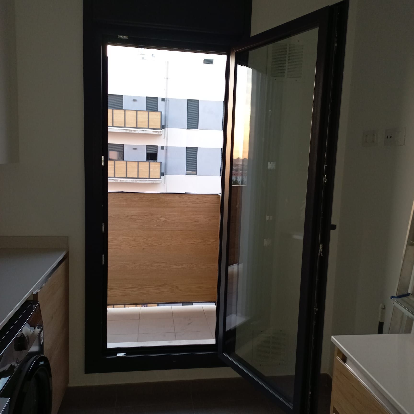 Una puerta de vidrio entreabierta conduce a un balcón con mosquitero marrón.