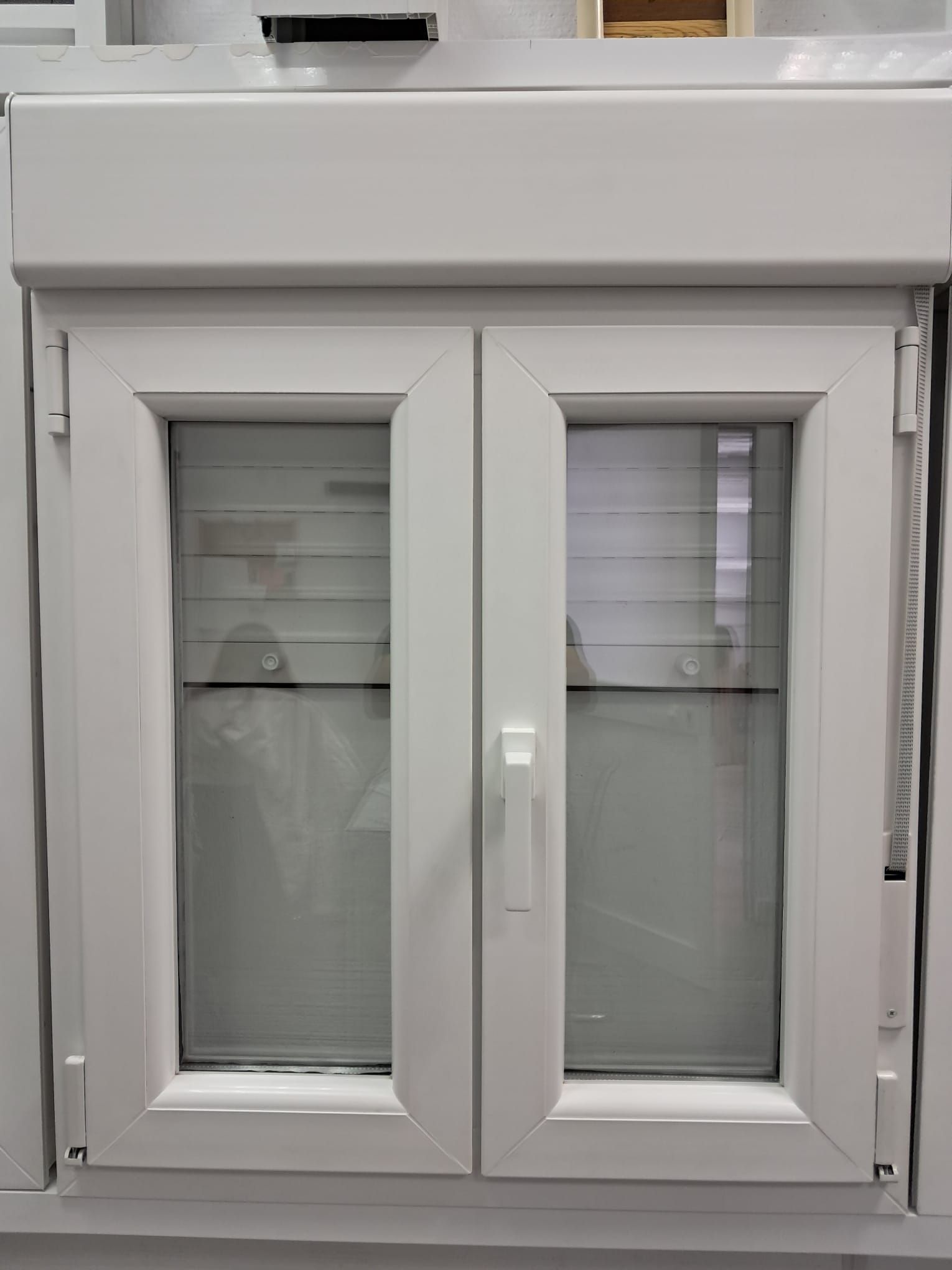 Ventana blanca de guillotina doble con persiana cerrada arriba y persianas mini en el interior.