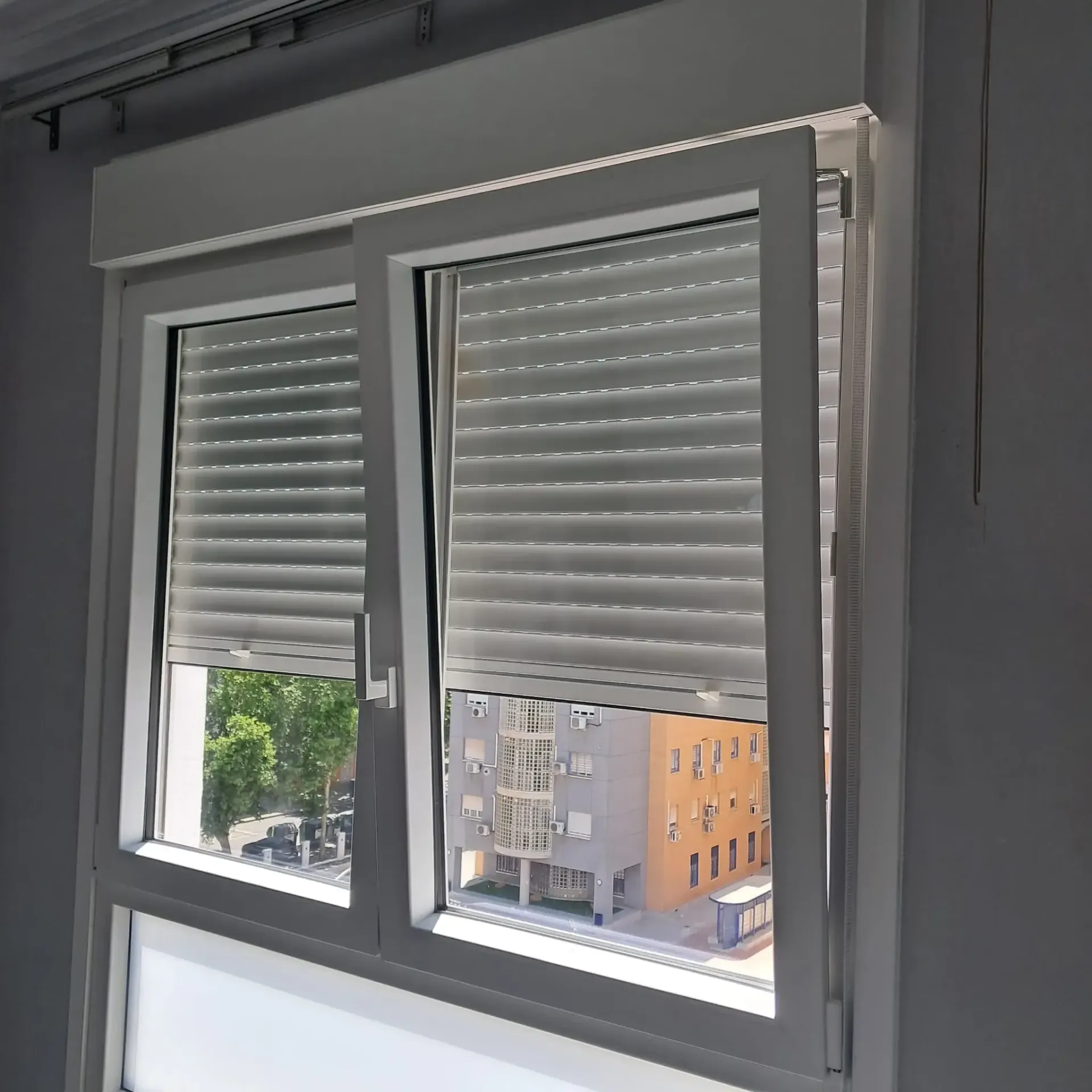 Ventana blanca con persianas cerradas, con vista a un edificio y a la calle.