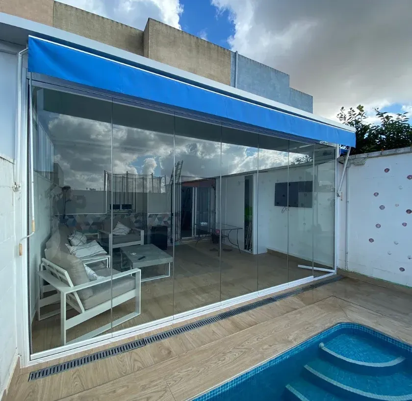 Hombre con camisa azul y gorra, usando un destornillador en la cerradura de una puerta. Pared de madera y puerta de cristal.