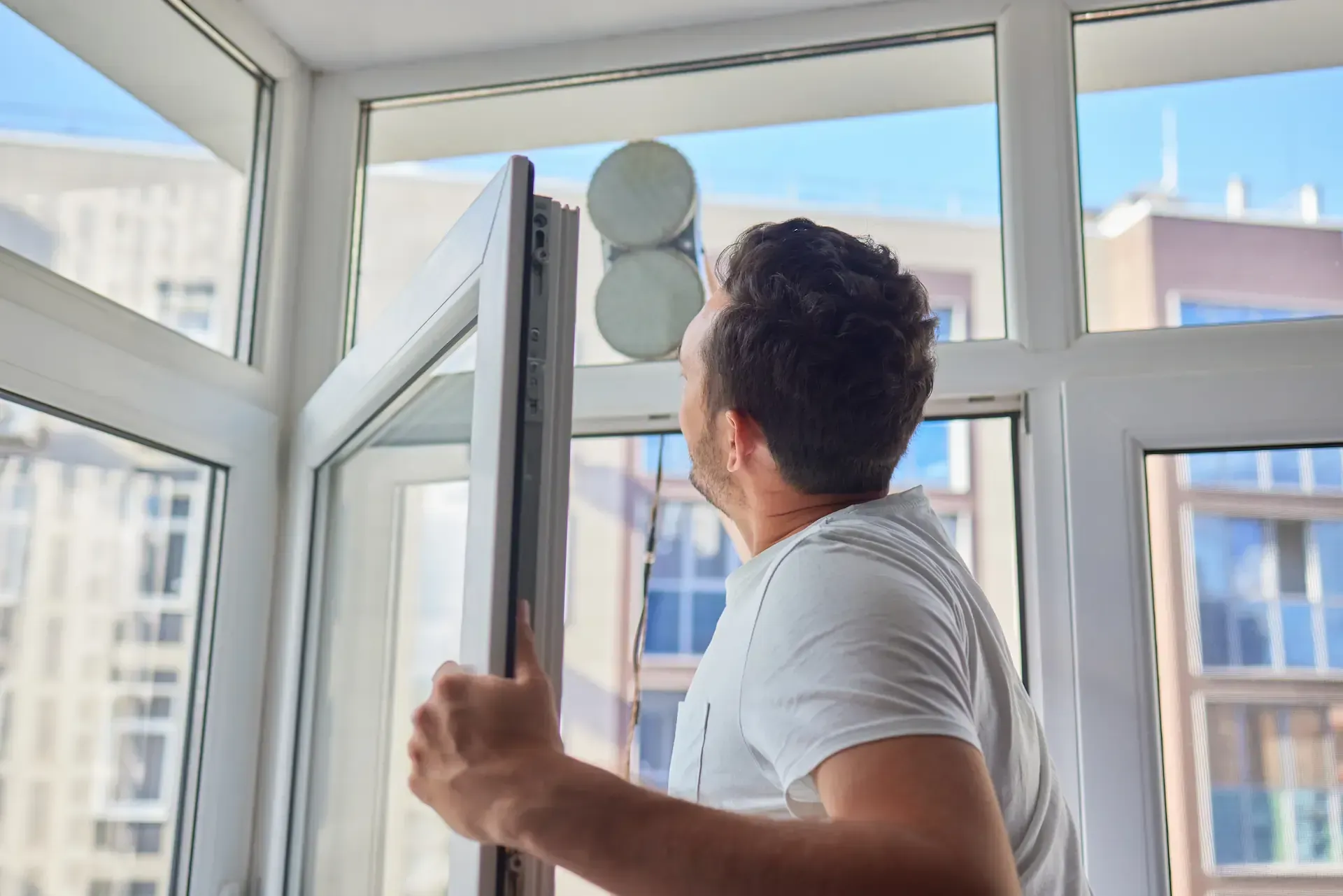 Hombre limpiando ventana con dispositivo robótico en balcón.