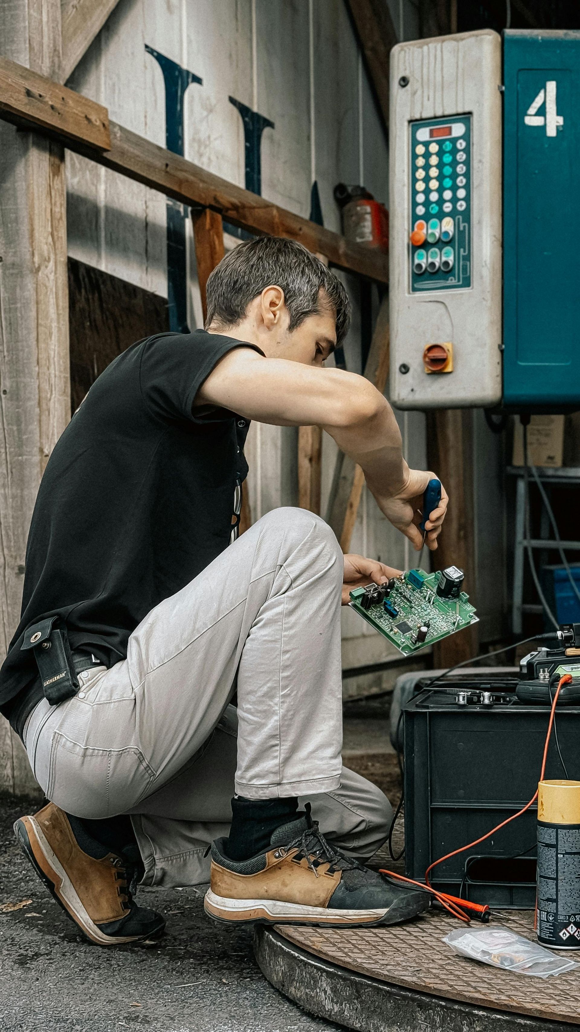 Hombre agachado, fijando placa de circuito con destornillador; entorno de taller.