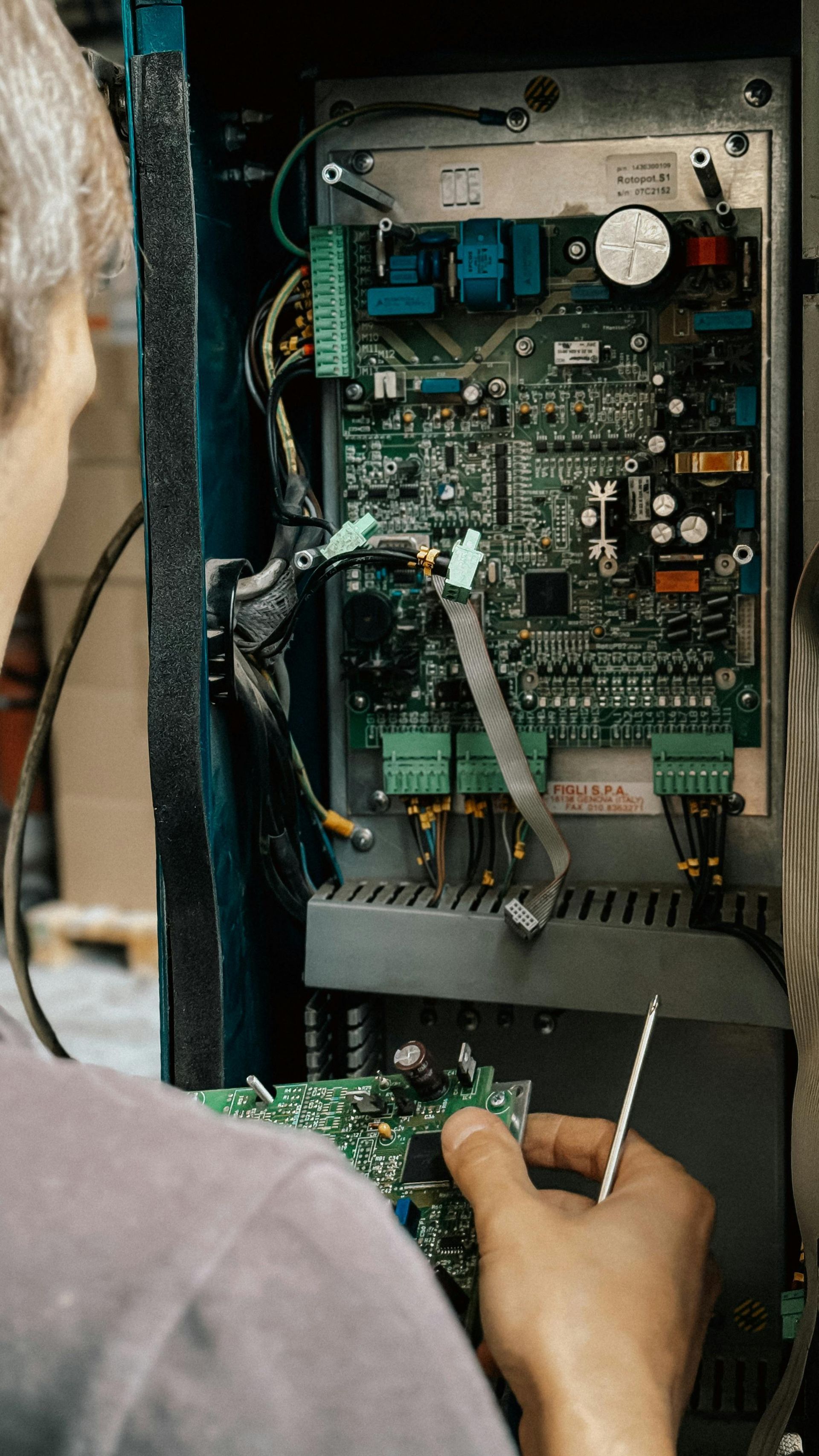 Persona reparando una placa de circuito dentro de un gabinete de metal azul con un destornillador.
