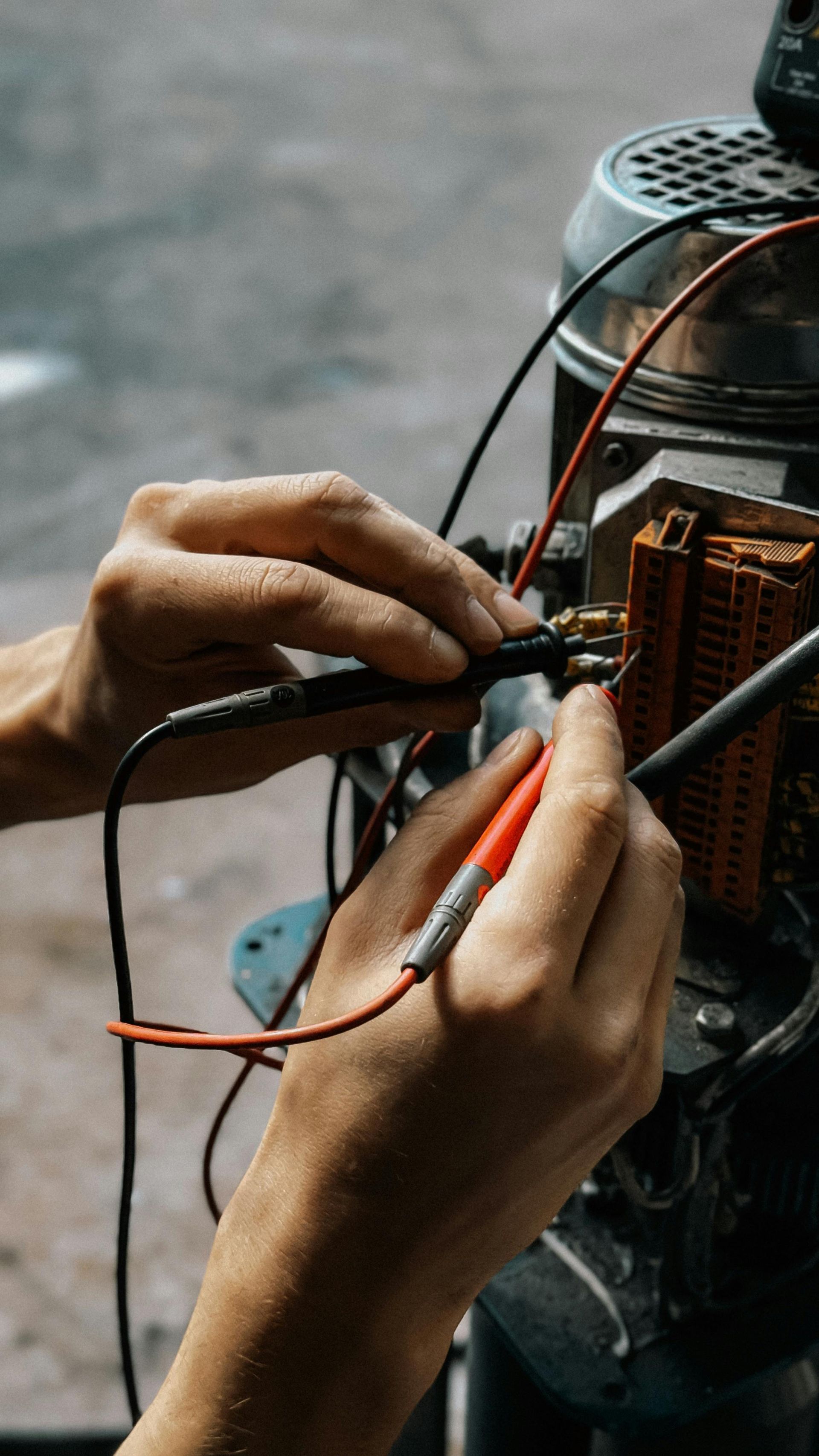 Manos usando un multímetro para probar el cableado de un motor, con cables negros y rojos visibles.