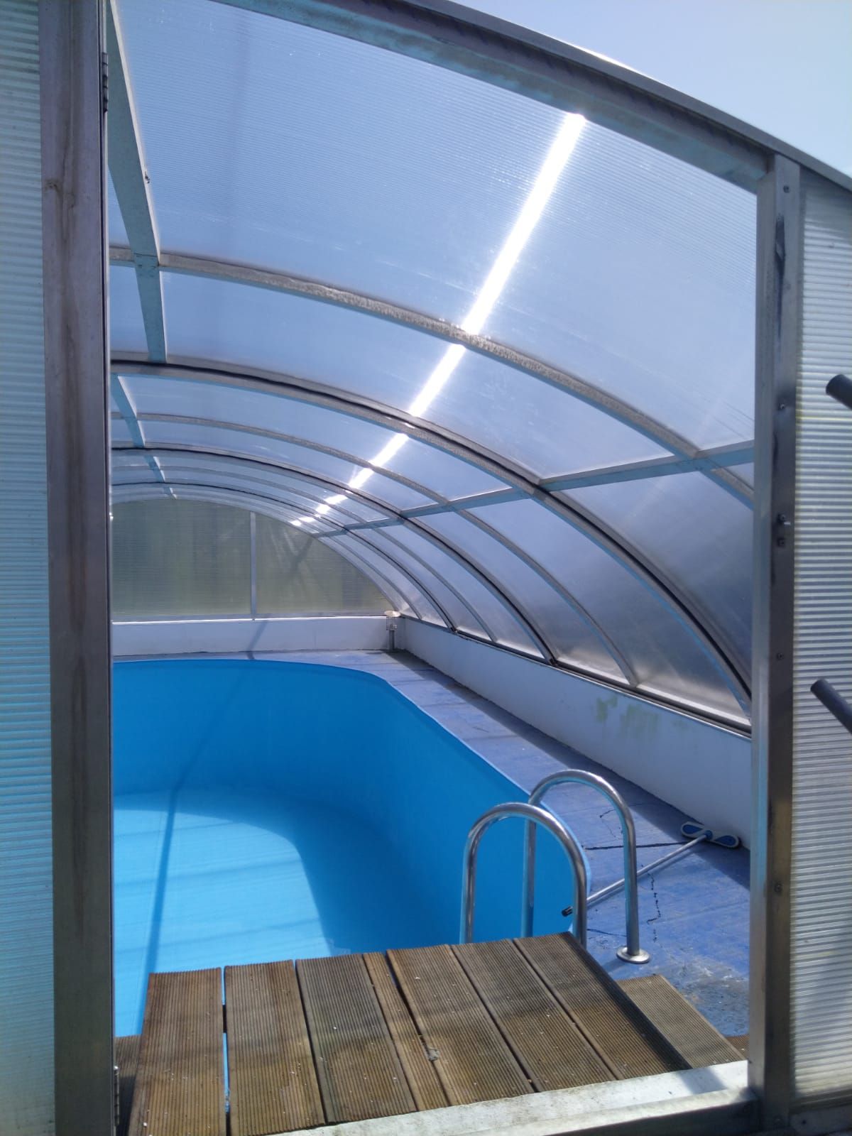 Ein Swimmingpool unter einem Baldachin mit Holzdeck und Treppe.