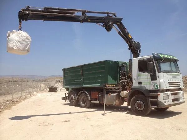 Un camión volquete con una grúa acoplada está estacionado en un camino de tierra.
