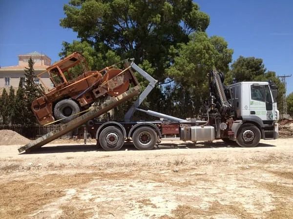 Un camión volquete transporta un vehículo oxidado en la parte trasera.