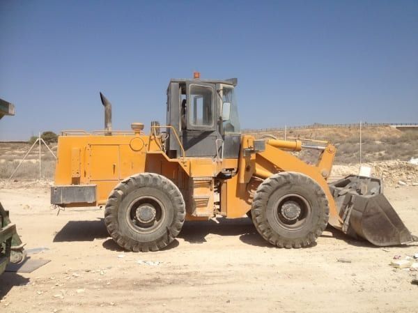 Una excavadora amarilla está estacionada en un campo de tierra