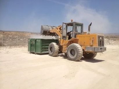 Una excavadora está cargando un contenedor verde en un campo de tierra.