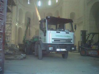 Un camión blanco está estacionado en un edificio con una carretilla elevadora al fondo.
