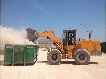Una excavadora está cargando un contenedor verde en un campo de tierra.
