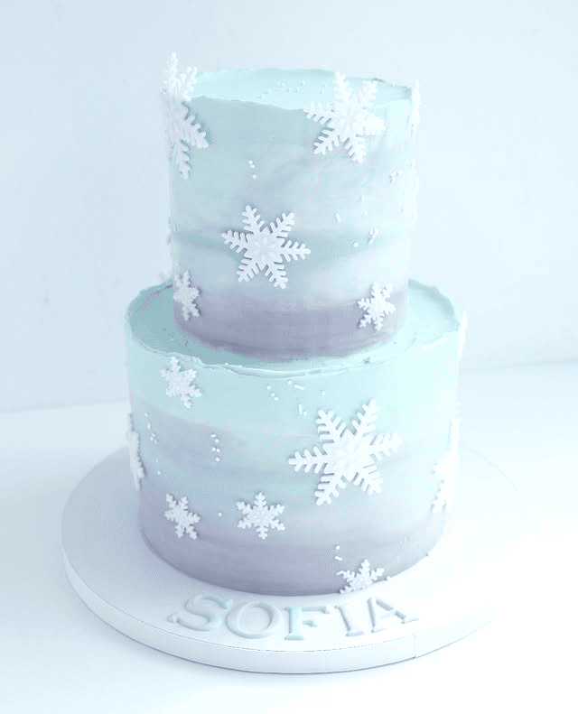 Un pastel azul y gris con copos de nieve encima está sobre un plato blanco.