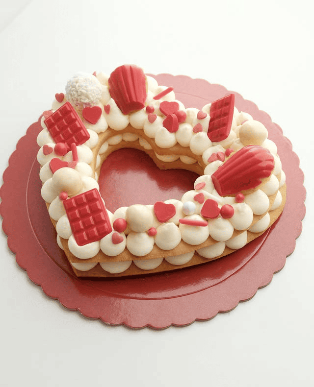 Un pastel en forma de corazón con glaseado blanco y corazones rojos.